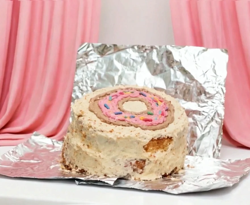 An uneven homemade cake with a clumsy pink donut piped on top.